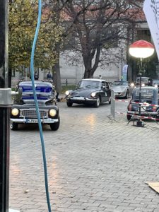 Auf dem Bild sind drei Oldtimer zu sehen, der vordere in dunkelblau, dahinter einer in dunklem grün