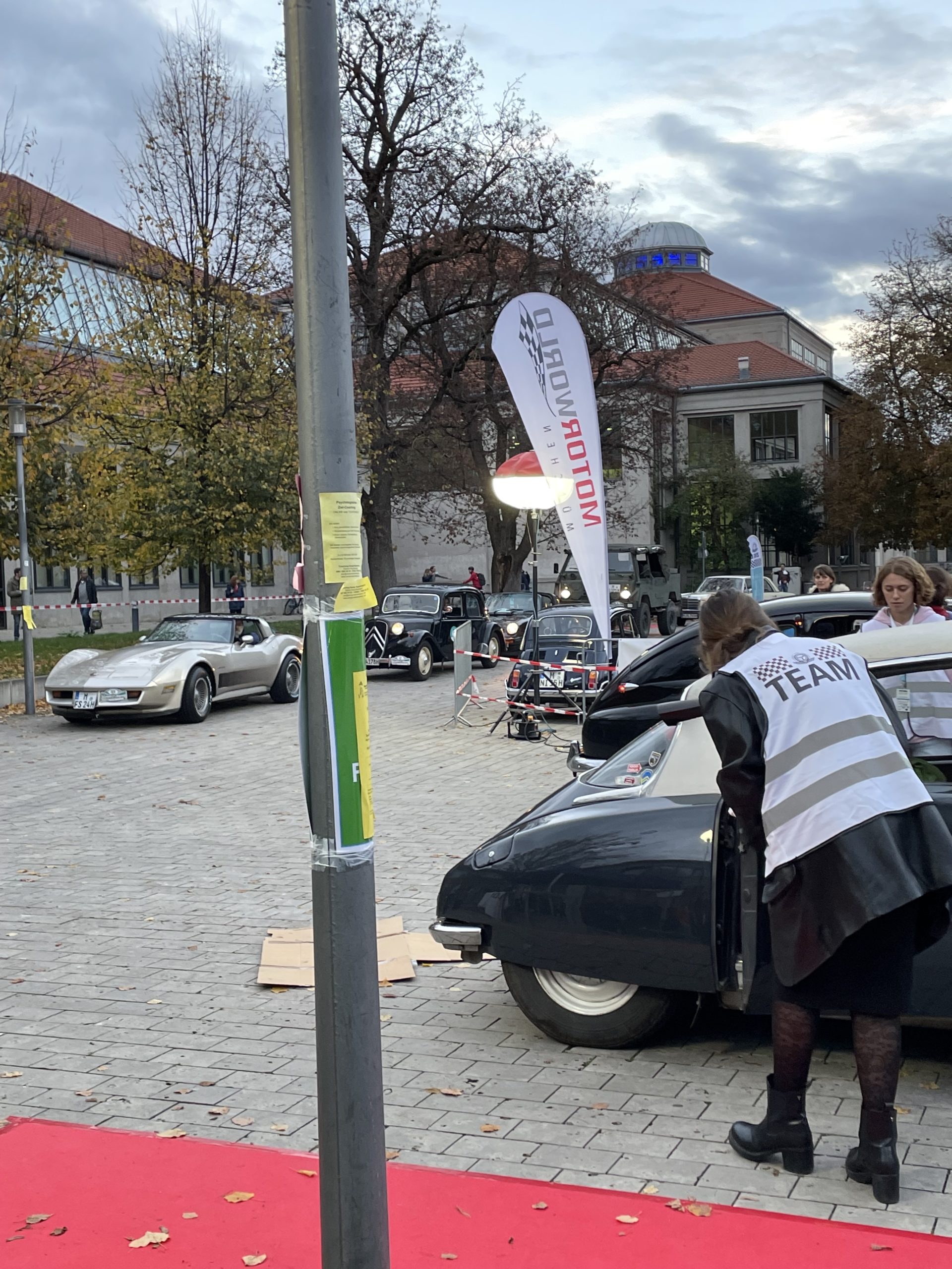 Im Vordergrund ein Teammitglied, welches in einen Oldtimer mit hellem Dach blickt, dahinter reihen ein altes Caprio in beige